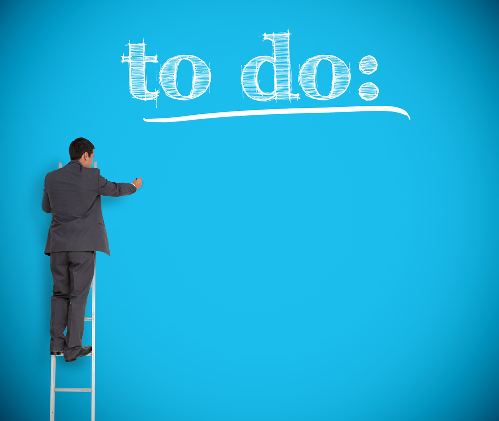 Businessman writing to do list on a giant blue wall helped by a ladder