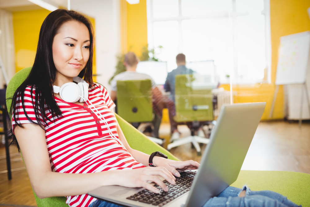 Happy young female executive using laptop at creative office