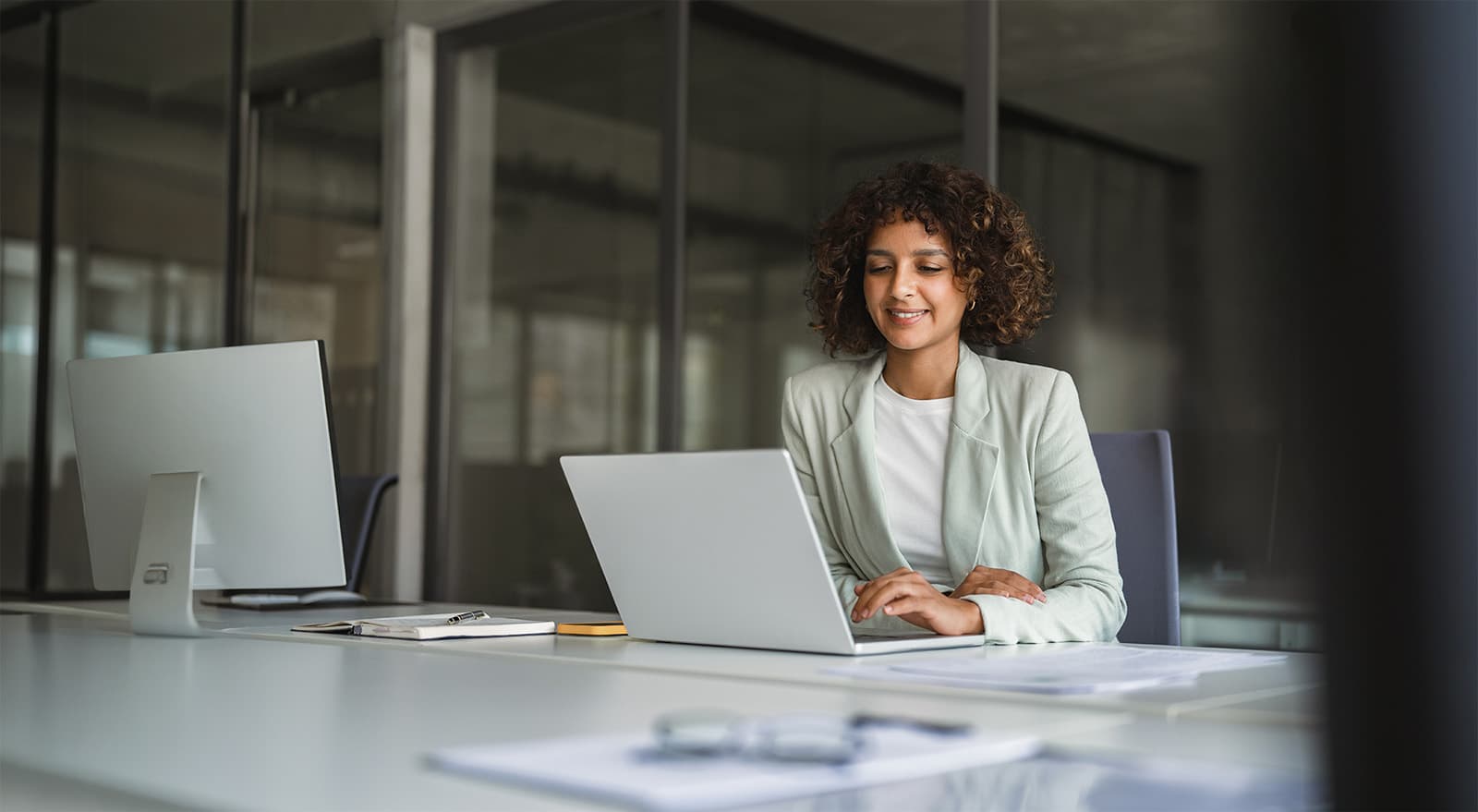 Young professional specialist latin hispanic businesswoman in suit working on laptop pc sitting at desk in office.